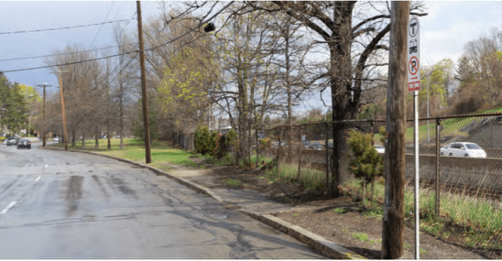A four-lane arterial street lined with trees with no sidewalk.