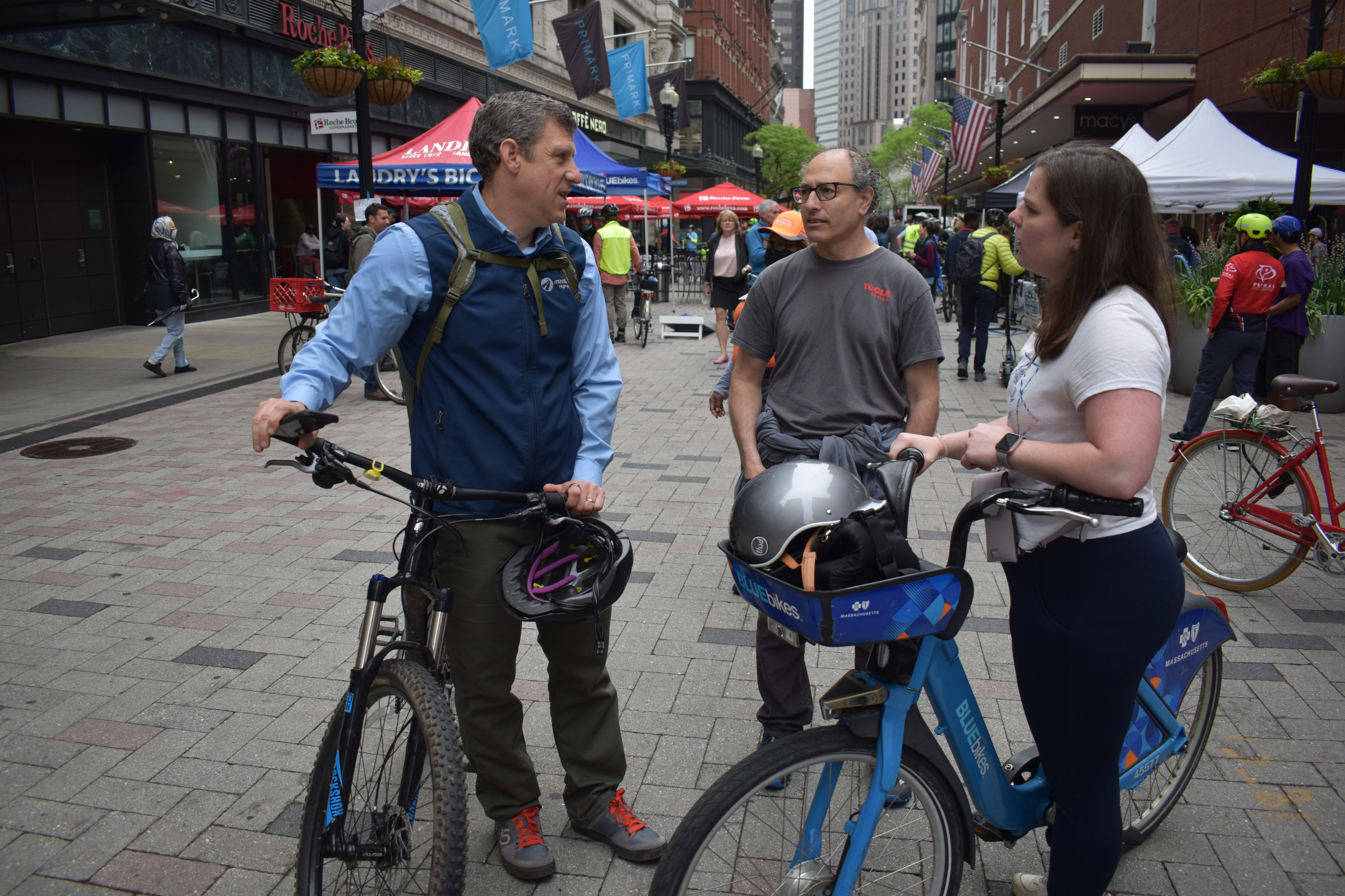 MassDOT Secretary Jamey Tesler, Jeff Rosenblum of Toole Design Group and Kirstie Hostetter, a transit planner with the City of Boston chat while holding their bikes in the middle of Summer Street in downtown Boston during the city's Bike to Work Day celebration. 
