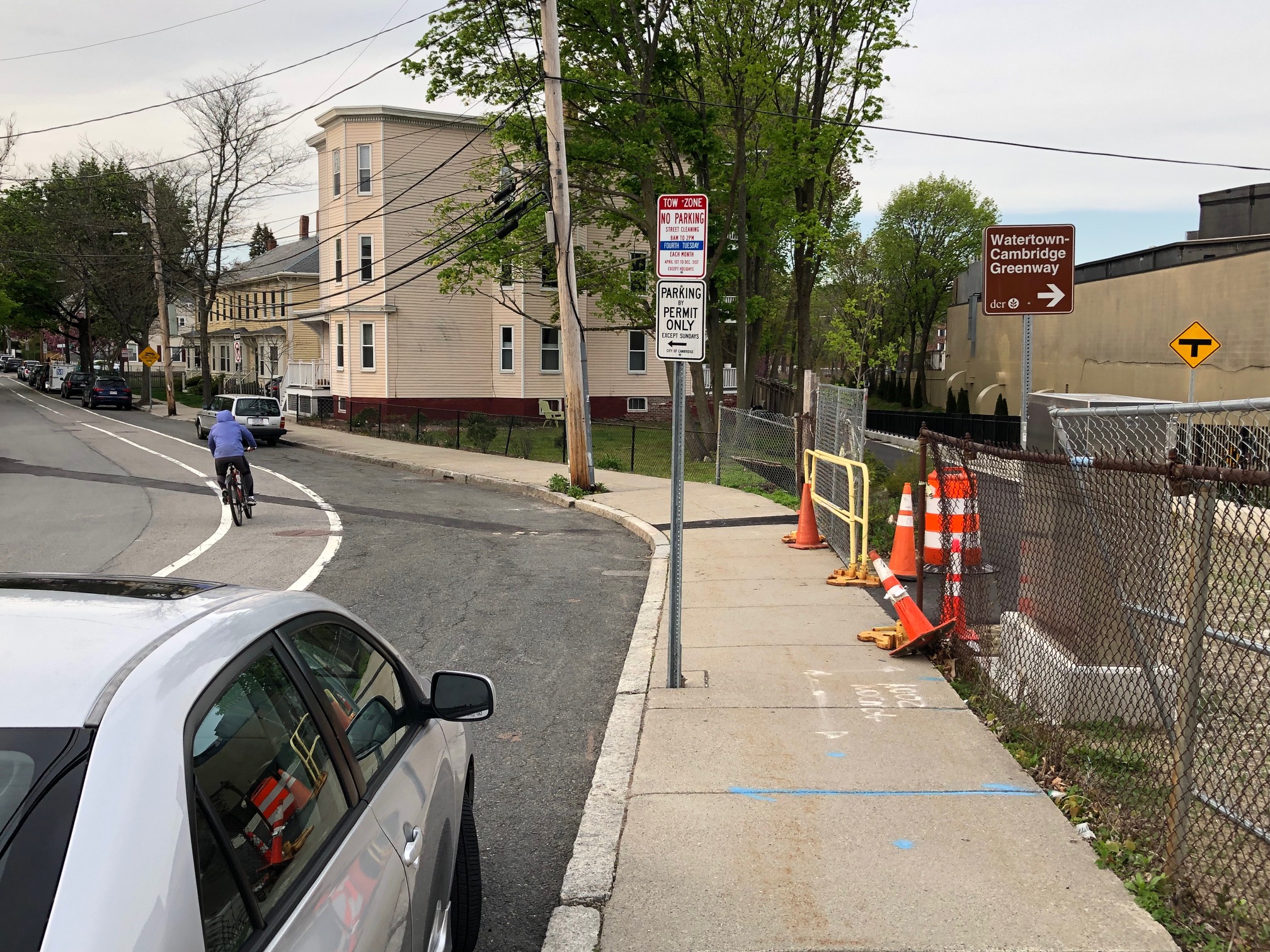 A trail entrance from Holworthy Street, near Mount Auburn Street, with a pile of construction cones and a sign indicating the "Watertown Cambridge Greenway."