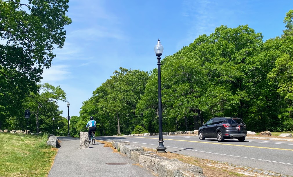 Woman riding a bike on the trail along Circuit Drive as a car goes by