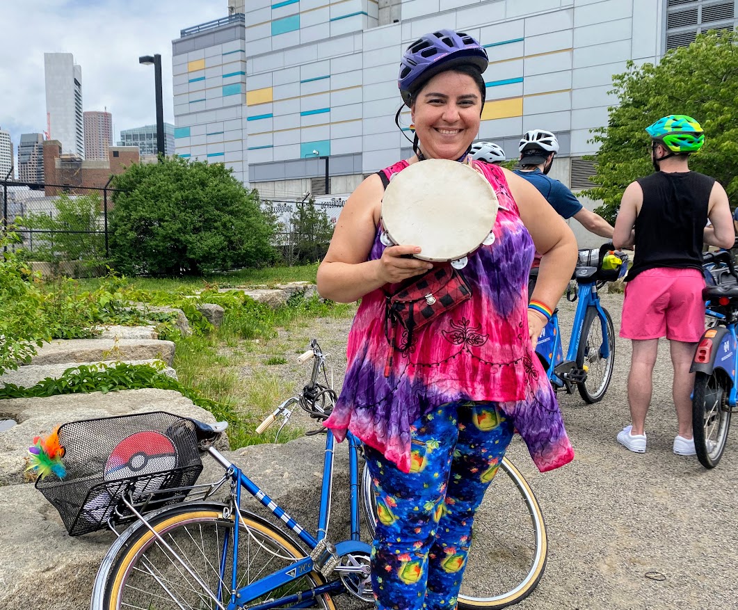 Ana posing with her tambourine in front of her blue bike.