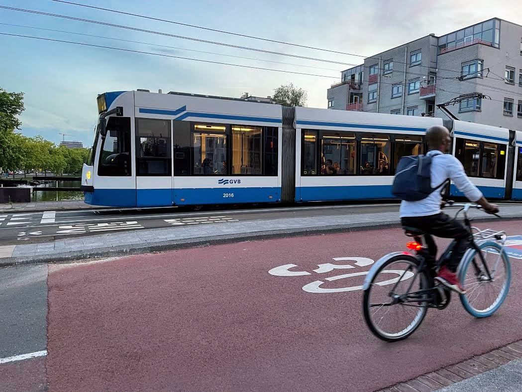 A bicyclist and a GVB tram pass each other in an Amsterdam street. GVB, Gemeente Vervoerbedrijf, is the municipal public transport operator in Amsterdam running the metro, tram, bus and ferry services.