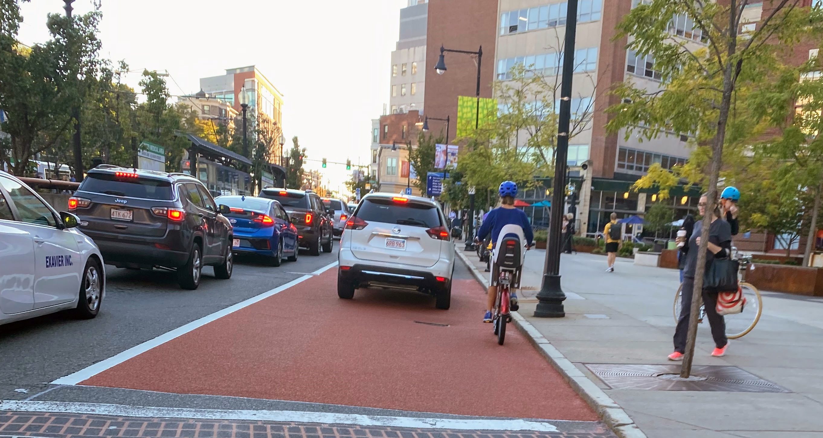 car traffic fills Huntington Avenue as pedestrians walk on the sidewalk and a bicyclists shares the bus and bike lane with a car