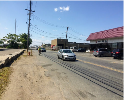 a bicyclist rides in between passing traffic and asphalt that merges into the nearby stretch of soil