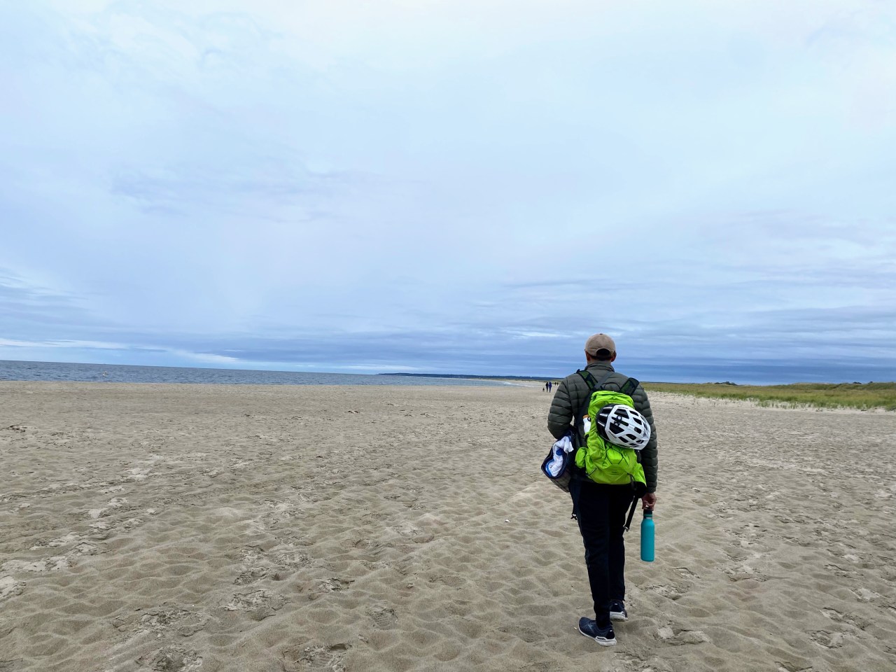 a sandy beach with the water in the far background and a grayish blue sky.