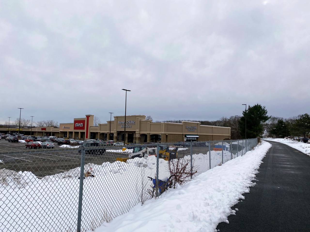 a clear trail on the left side of a fence separating it from a large shopping center.