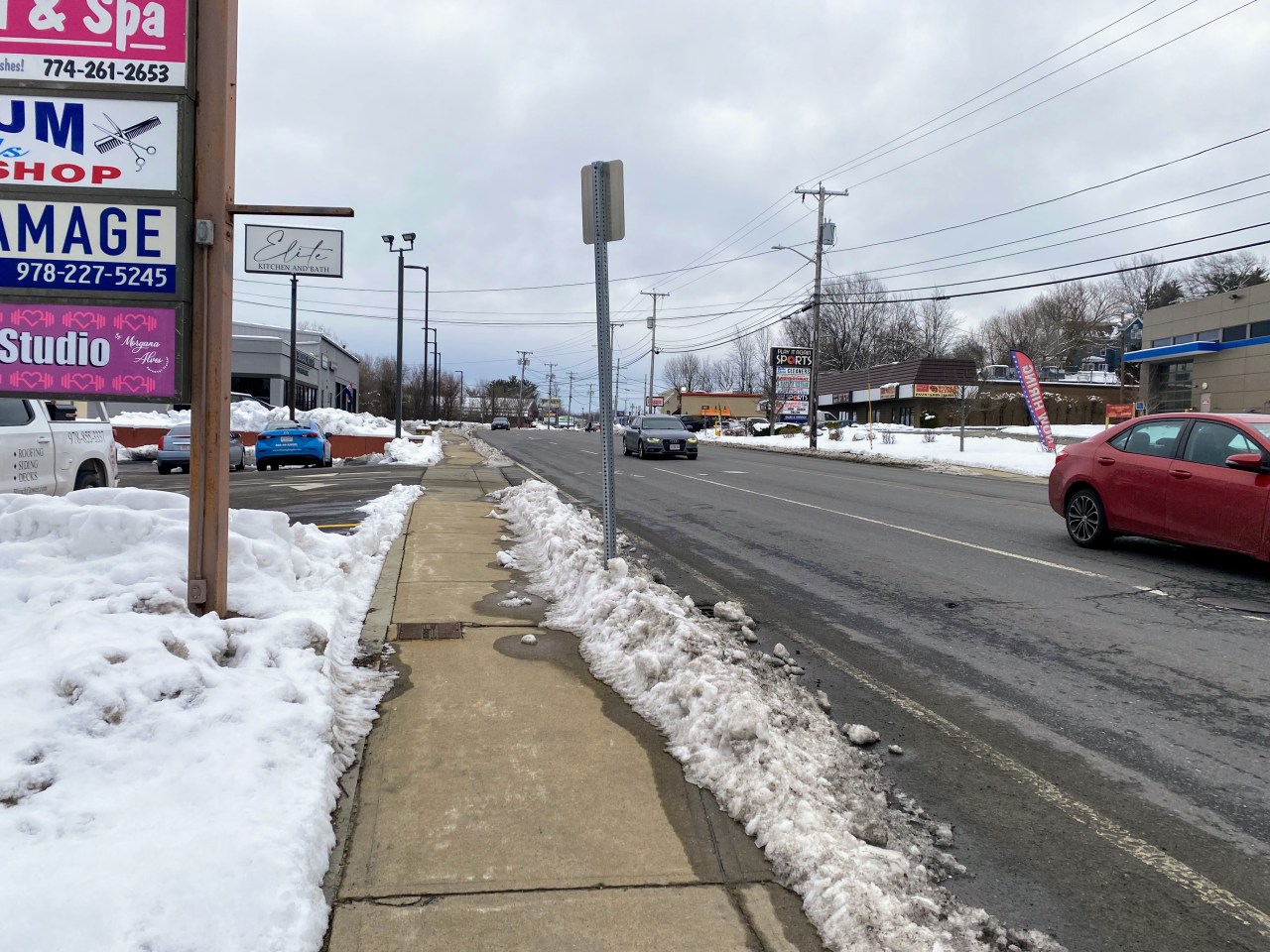 a sidewalk lined with snow banks next to a wide road.