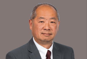 Phillip Eng headshot: a middle-aged man with close-cropped hair wearing a dark grey suit and red tie.