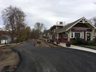 A wintertime photograph of a fresh coat of pavement on a trail alongside an old railroad station. 