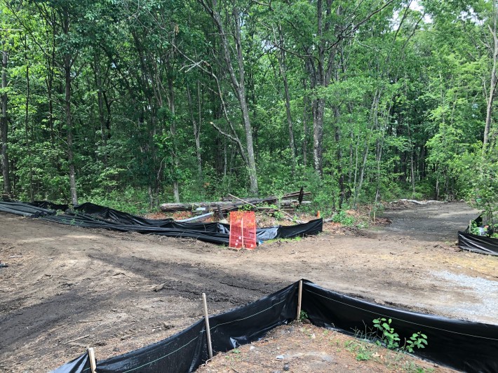 Two dirt roads meet at a 90-degree angle in the woods. The roads are lined with pipes and black erosion-control fencing.