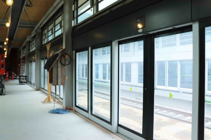 Glass doors in a transit station construction site. Rails are visible on the other side of the doors.