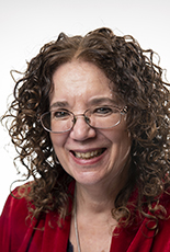 A headshot of a smiling white-skinned woman with shoulder-length curly hair and glasses.