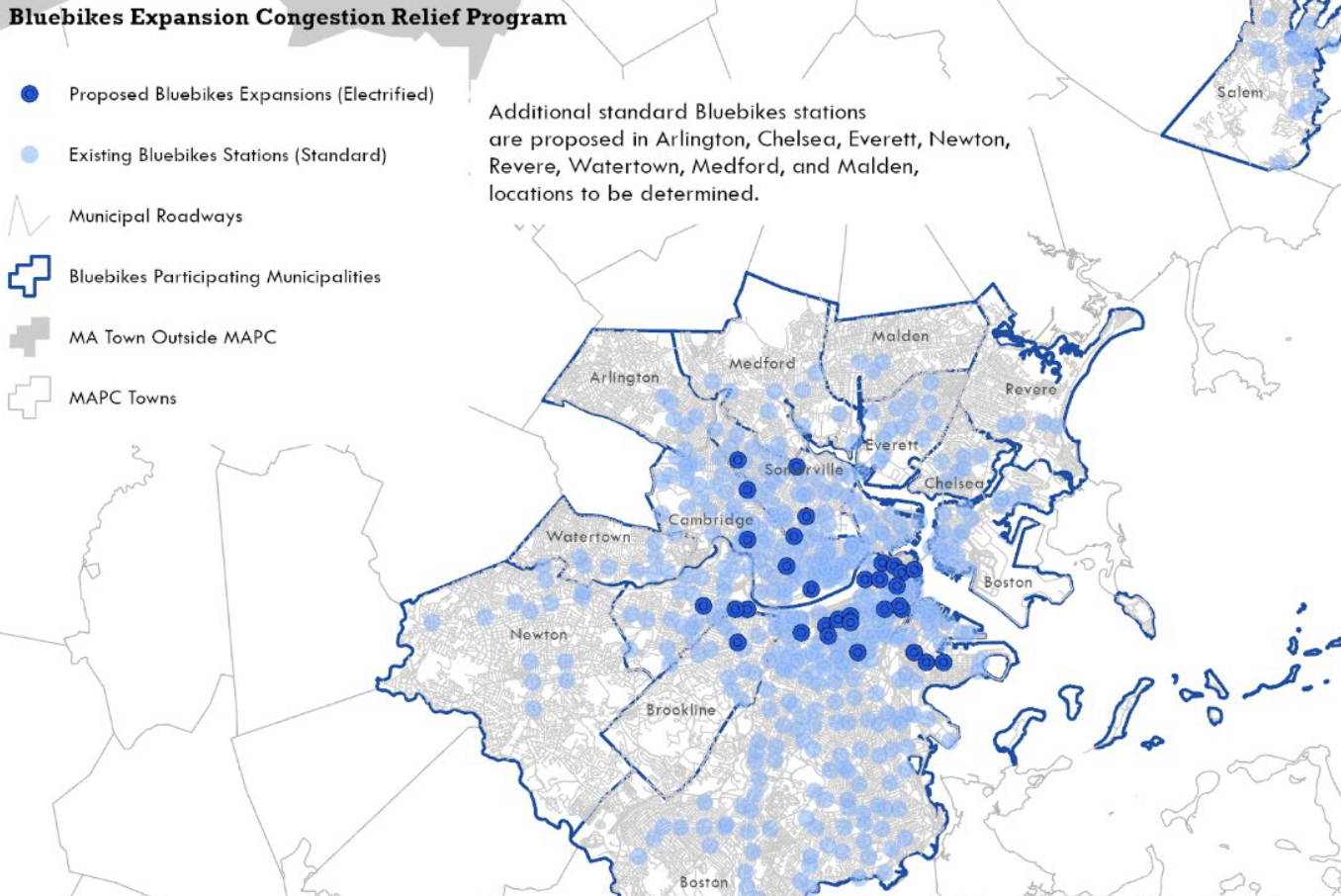 A map of the Bluebikes service area in greater Boston showing Bluebikes stations as pale blue dots. A cluster of darker blue dots in the core of the region – in Cambridge and Somerville, and the Back Bay and downtown neighborhoods of Boston – indicate the proposed locations of new electric docks for recharging e-bikes. 