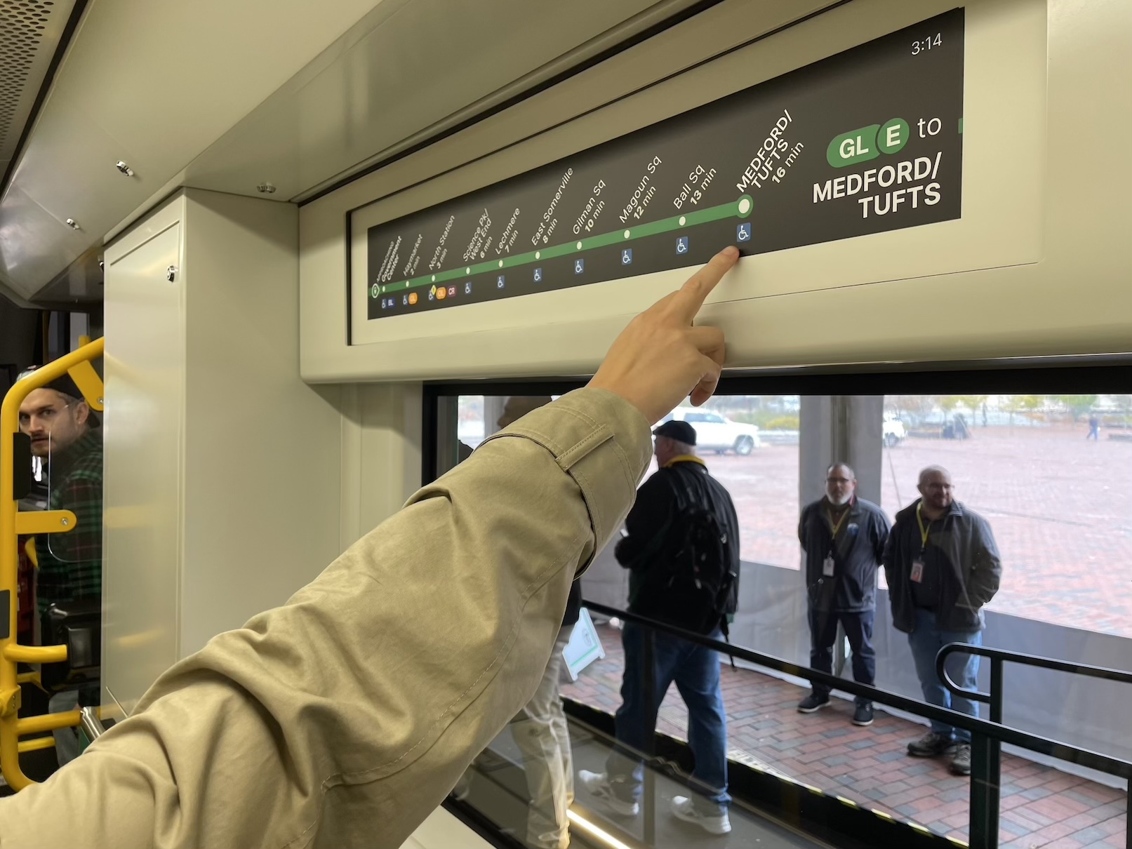 Someone points to a strip map showing part of the MBTA Green Line on a screen above the window of a train car.