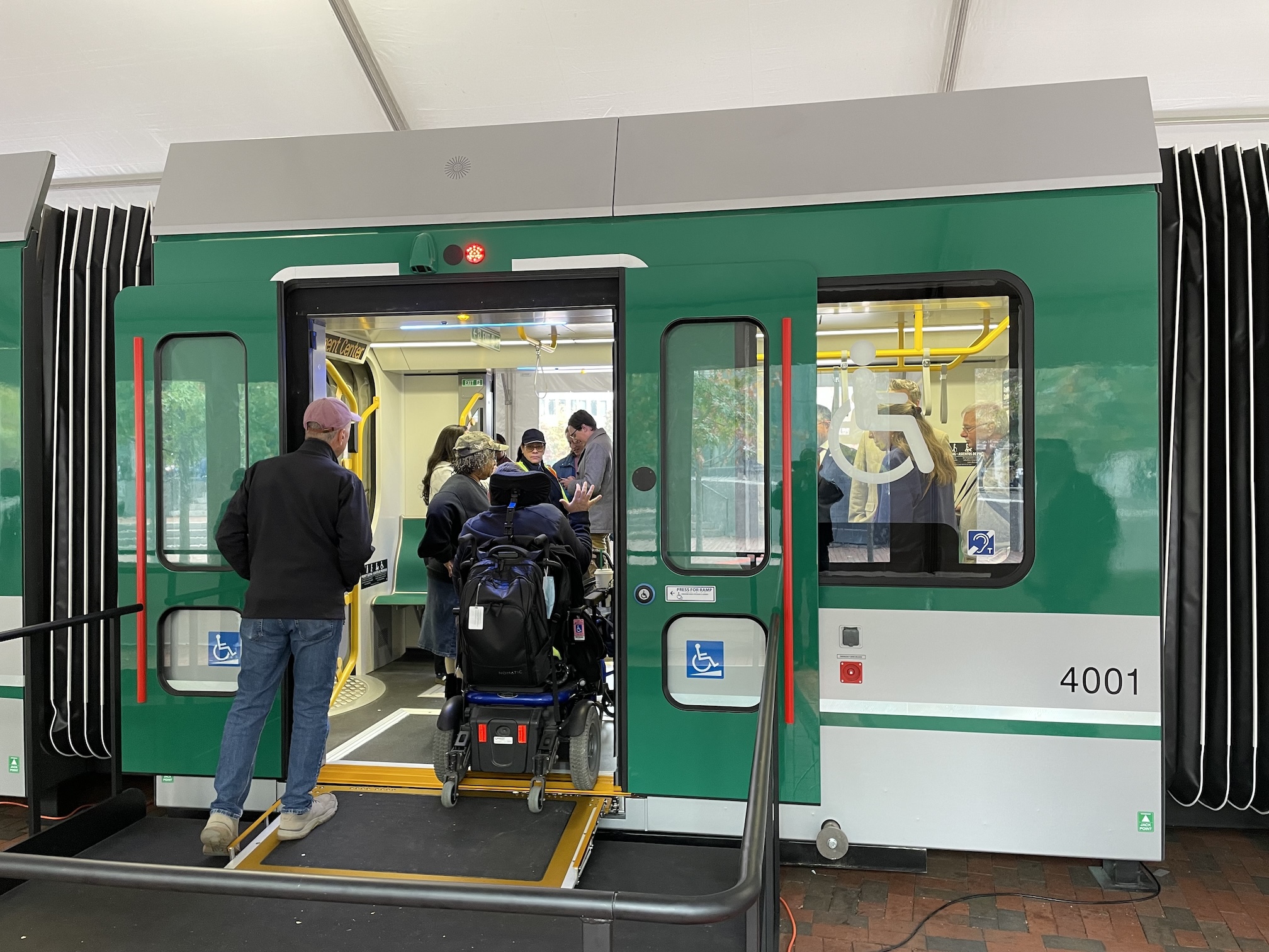 A person in a wheelchair uses a small ramp to cross the threshold of a MBTA Green Line train next to a window with a large wheelchair icon.