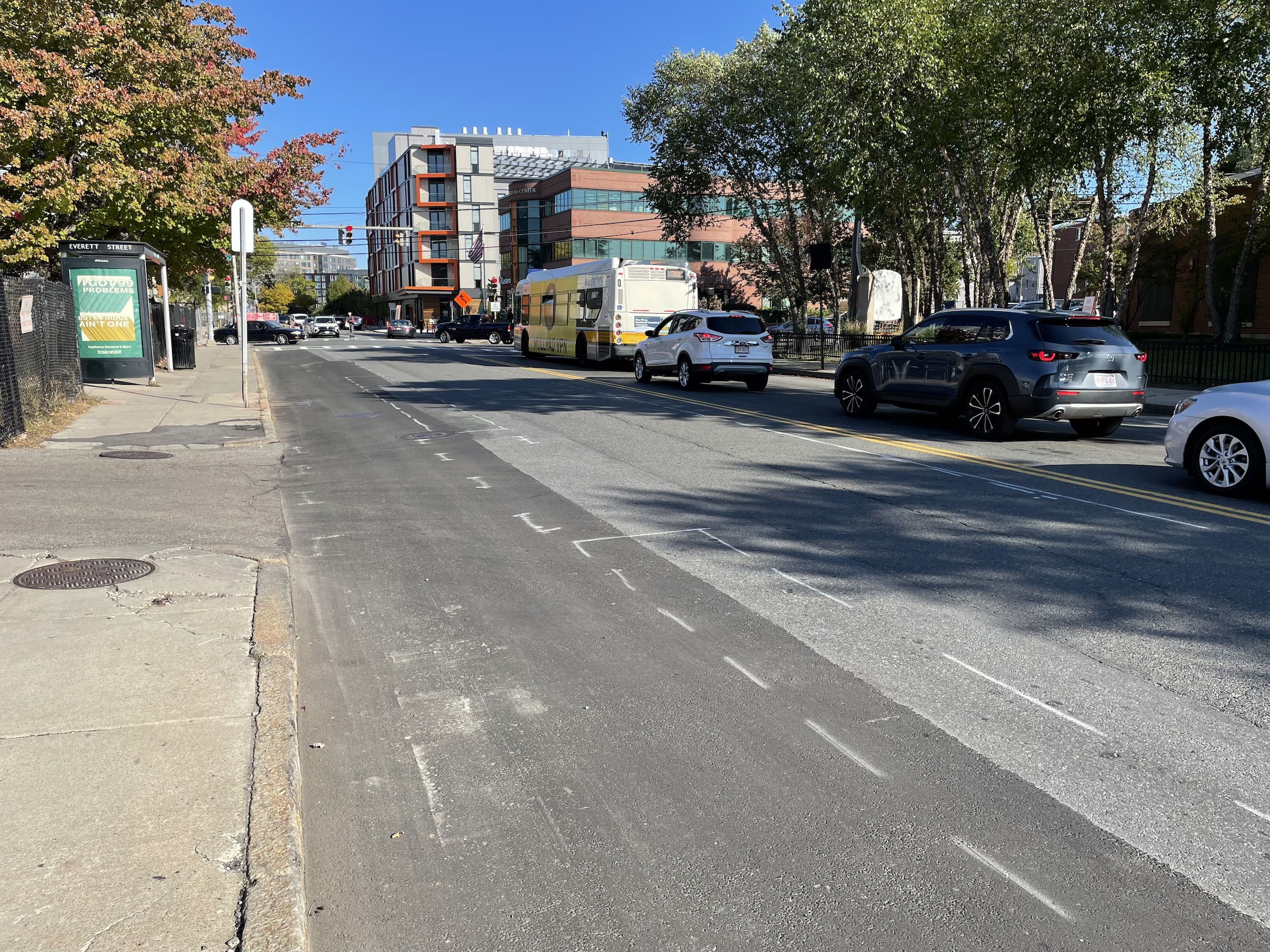 A city street and traffic signal in the distance with a row of cars waiting for the light. Spray-painted markings outline a future bike lane in the foreground.