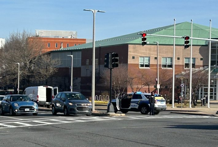 A police officer stands next to a police car parked under a traffic light in a wide multi-lane intersection