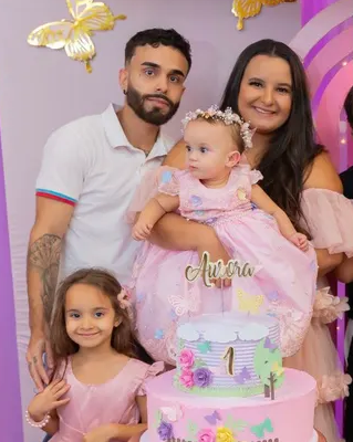 A young family poses with a pink birthday cake for a baby in a pink dress.
