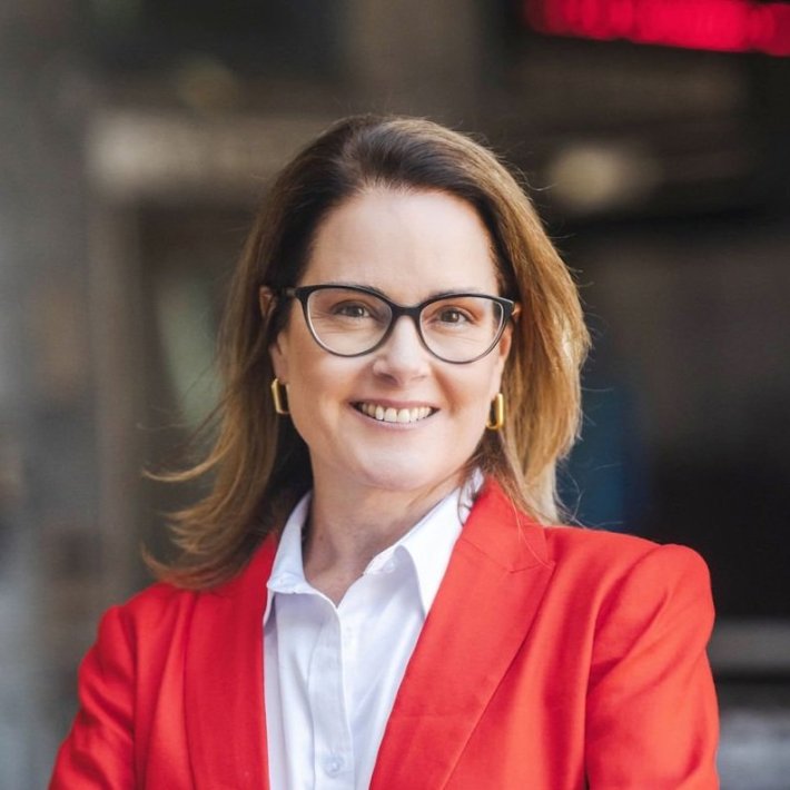 A white woman with shoulder-length brown hair wearing glasses and a red blazer