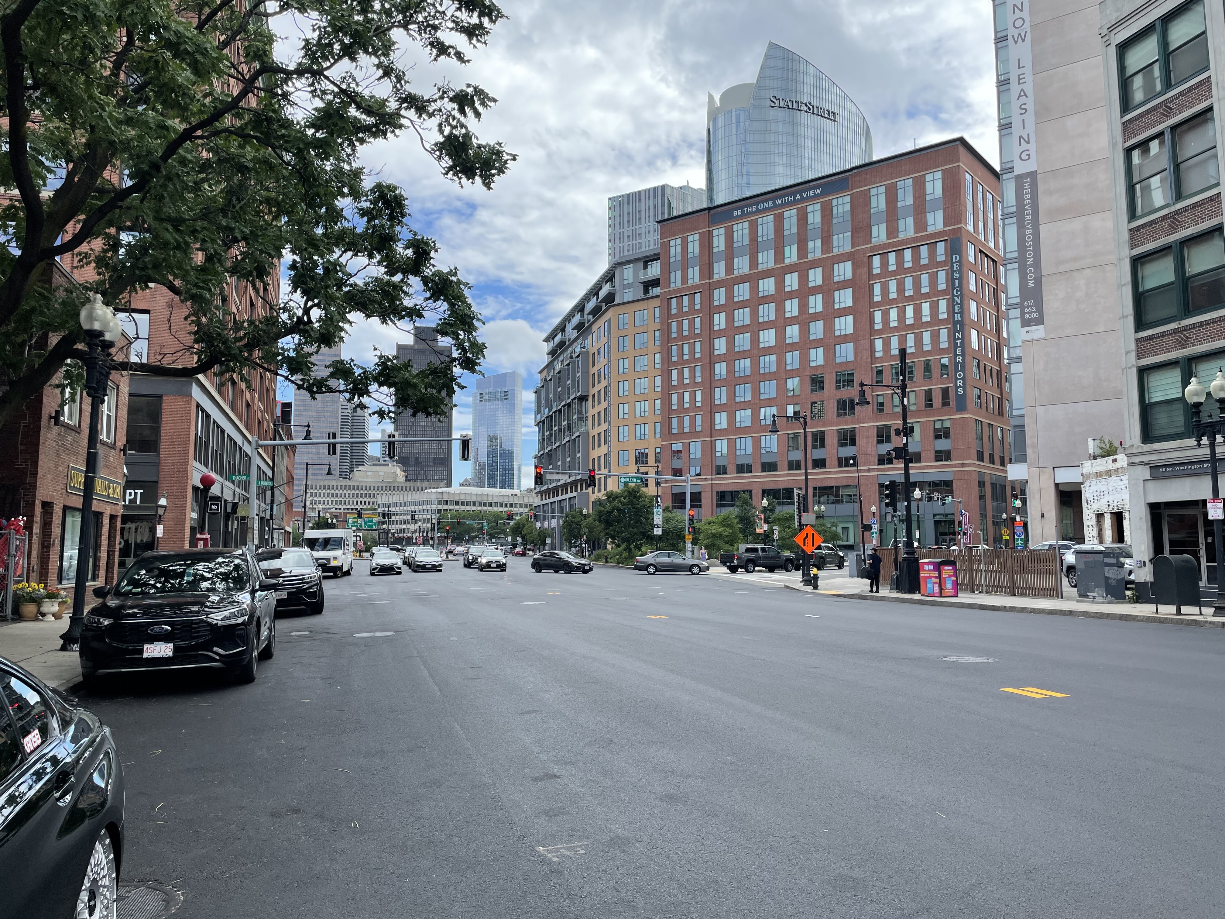A wide city street with fresh asphalt and no painted lane markings. In the background are several high-rise buildings