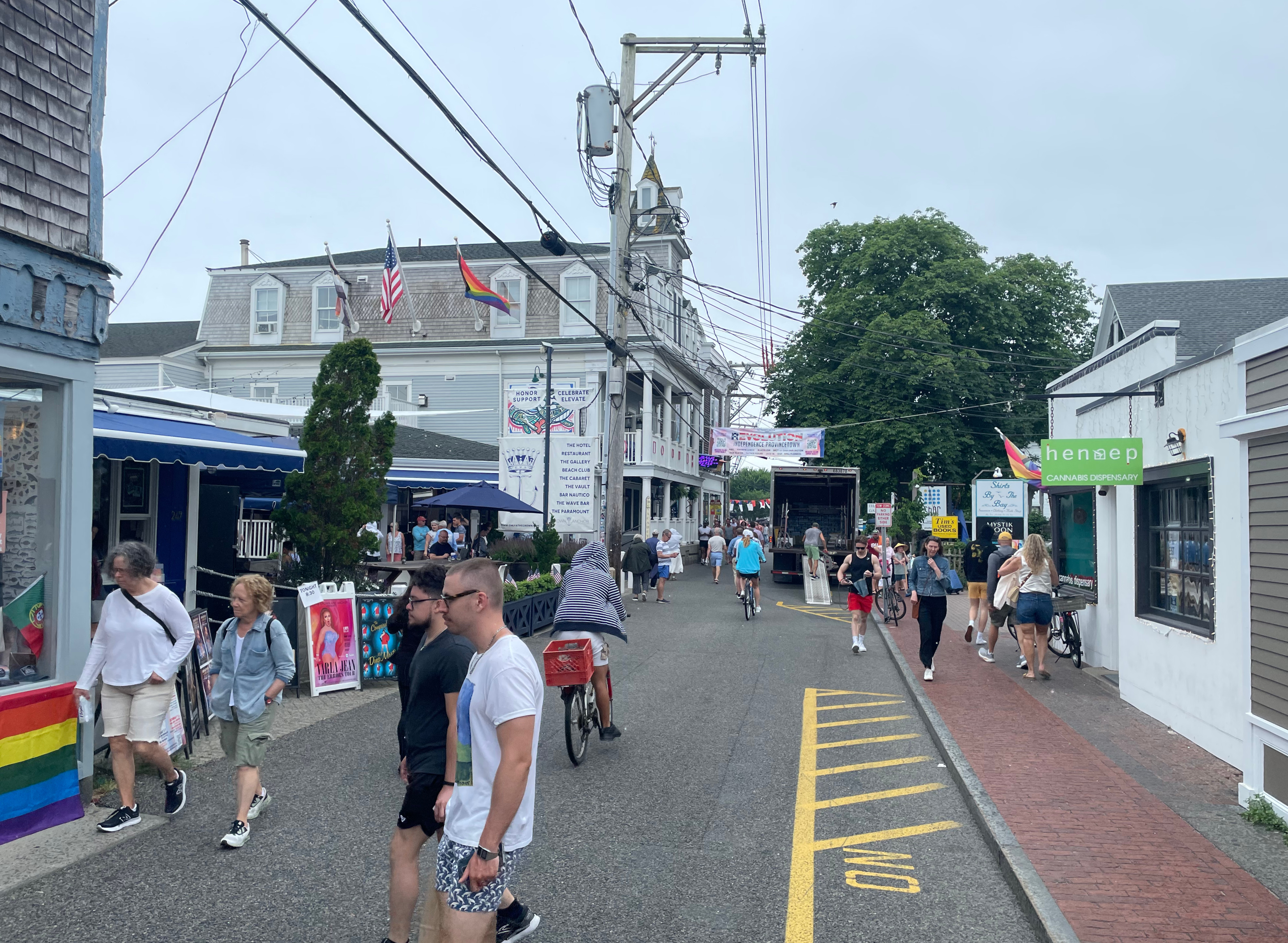Pedestrians fill a narrow street lined with two-and three-story retail buildings. There's a narrow brick sidewalk on the right edge of the street.