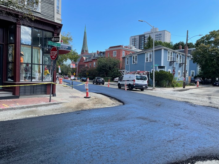 Freshly laid asphalt on a street that's otherwise surfaced in dirt through the middle of a city neighborhood. 