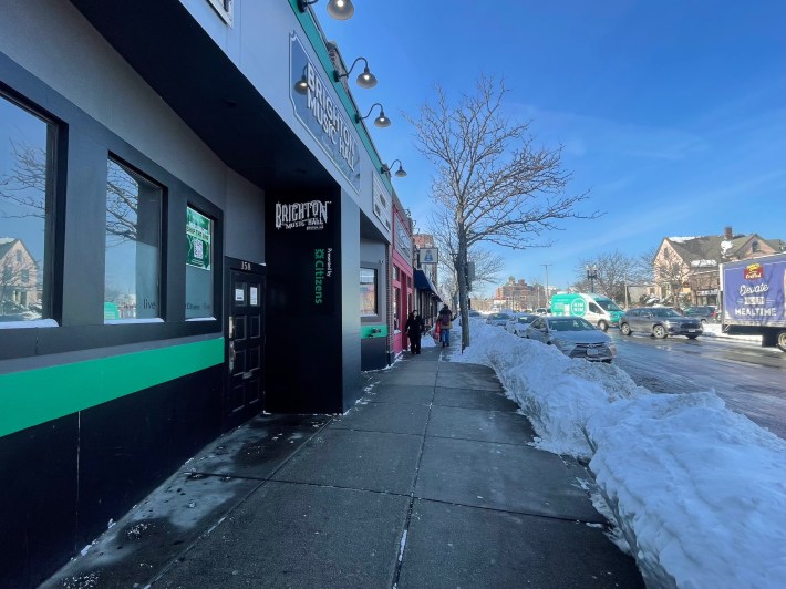 A well-cleared sidewalk in winter next to a one-story building (left) and a large snowbank (right)