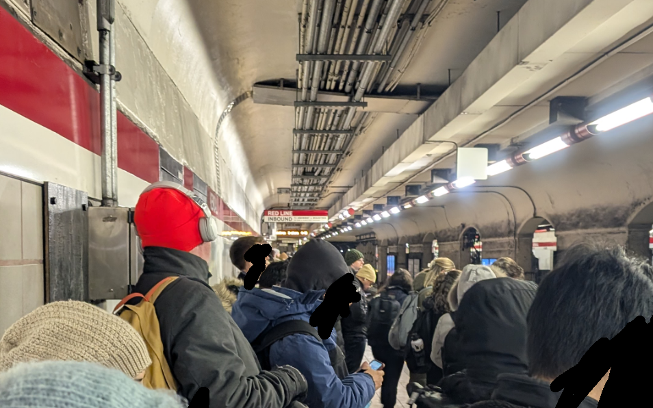 Crowds of people in winter coats pack the platform of a Red Line subway station.