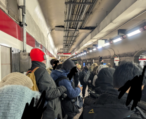 Crowds of people in winter coats pack the platform of a Red Line subway station.