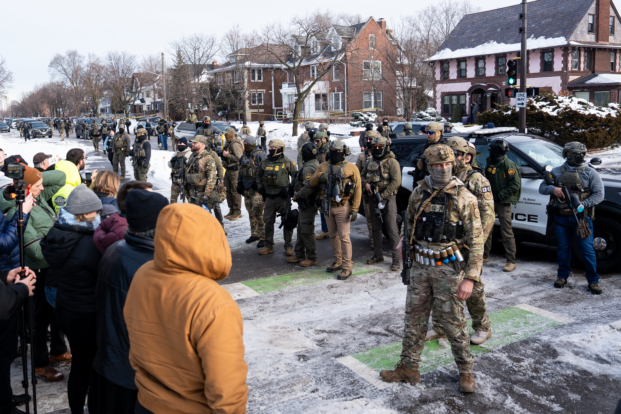 A row of armed masked police in confront a row of protesters on a snowy winter street.