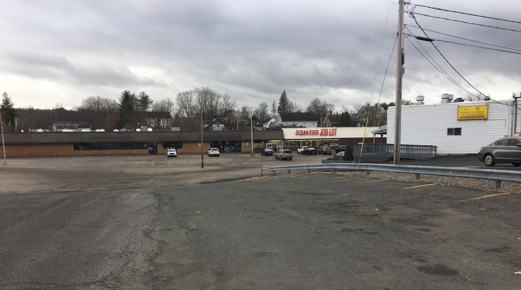 A large strip mall parking lot. In the distance is a single-story strip mall with a sign that says "Ocean State Job Lot"