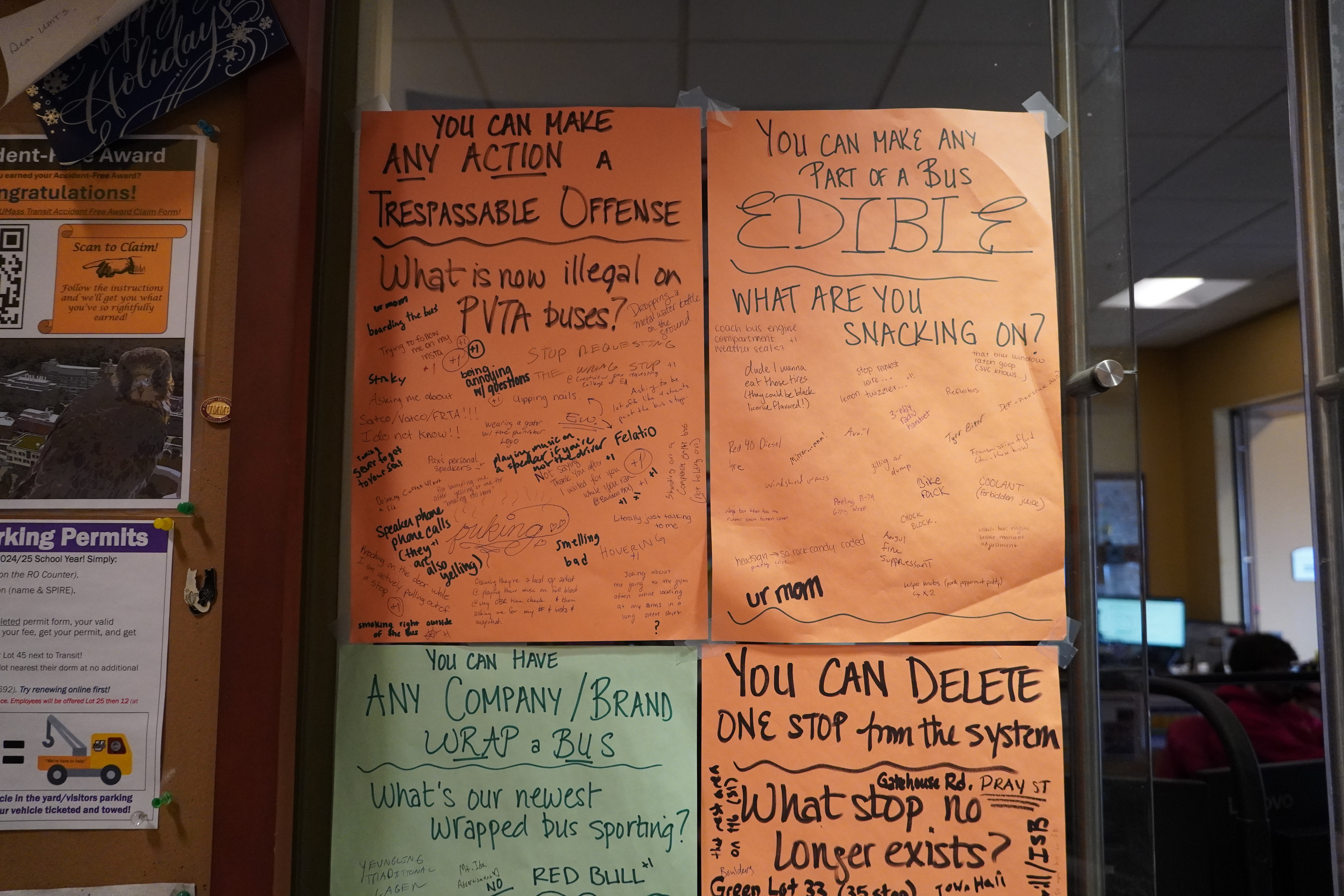 Posters hung from a wall on colorful paper, filled with handwriting from different people. The poster in the upper left is titled "What is now illegal on PVTA buses" with responses like "smelling bad," "being annoying with questions" and "trying to follow me on my insta." The upper right poster reads "you can make any part of a bus edible, what are you snacking on?" with responses like "red 40 diesel," "chock block" and "ur mom"