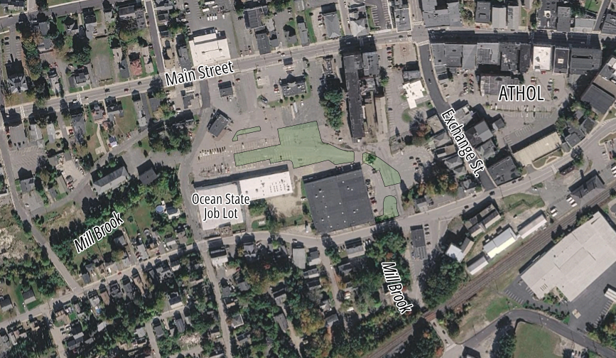A satellite view of a small town's downtown district with a strip mall surrounded by a large parking lot in the center and a street labelled "Main Street" lined with smaller buildings running along the top of the image. 