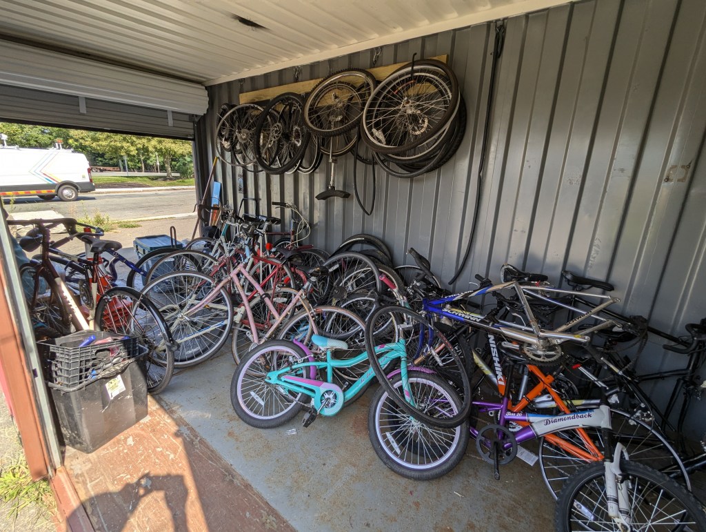 Inside of a shipping container packed with dozens of bicycles of various sizes, and a row of bike wheels hanging from the metal wall.