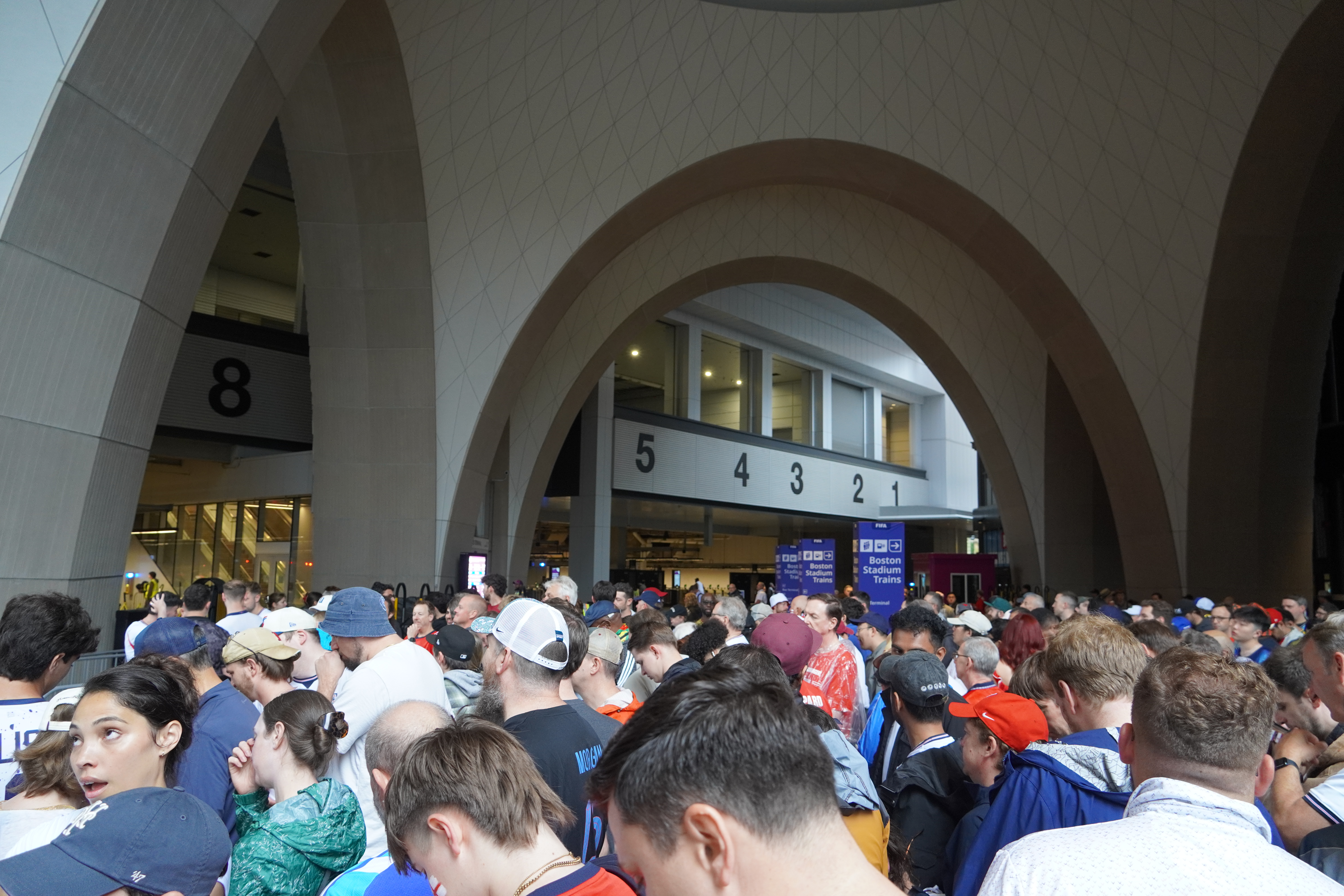 A crowd of soccer fans fills the waiting area of a train station under tall arched vaults.