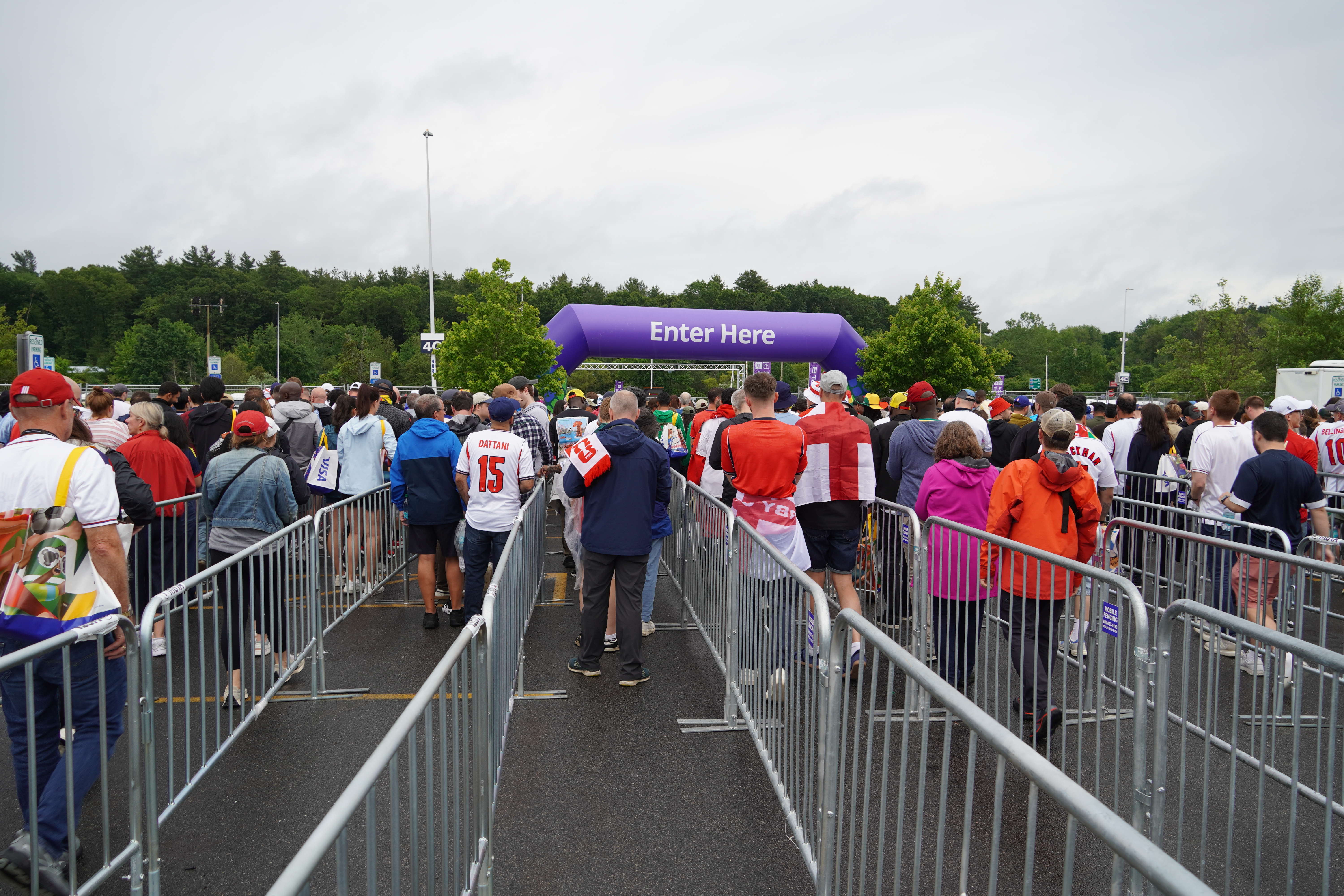 A crowd of people waits in front of an inflatable purple arch labelled "Enter Here" among corrals of metal fencing.