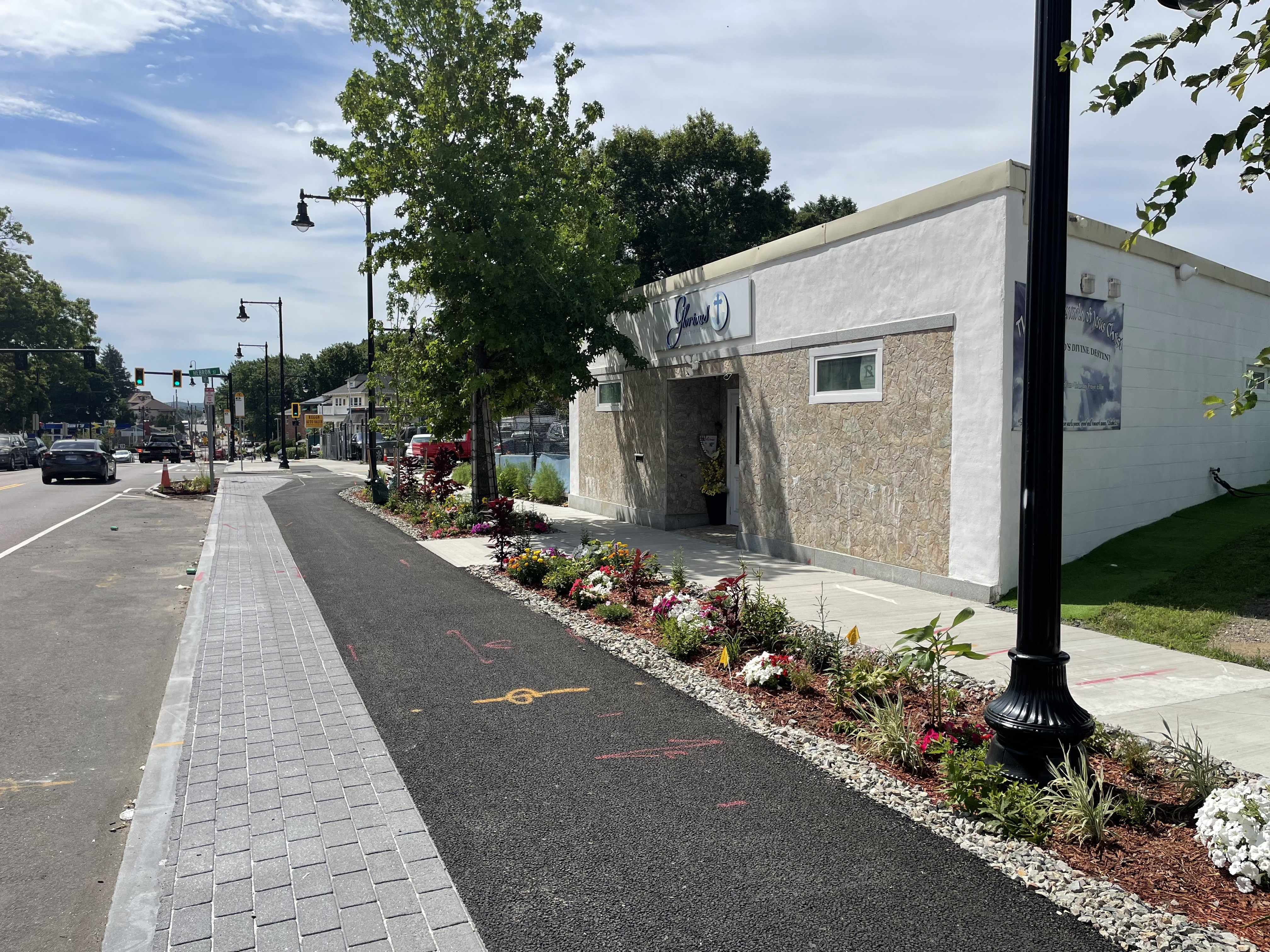 A curb-protected bike lane runs past a one-story church building with lots of flowers planted in the buffer space between the bike lane and the sidewalk.