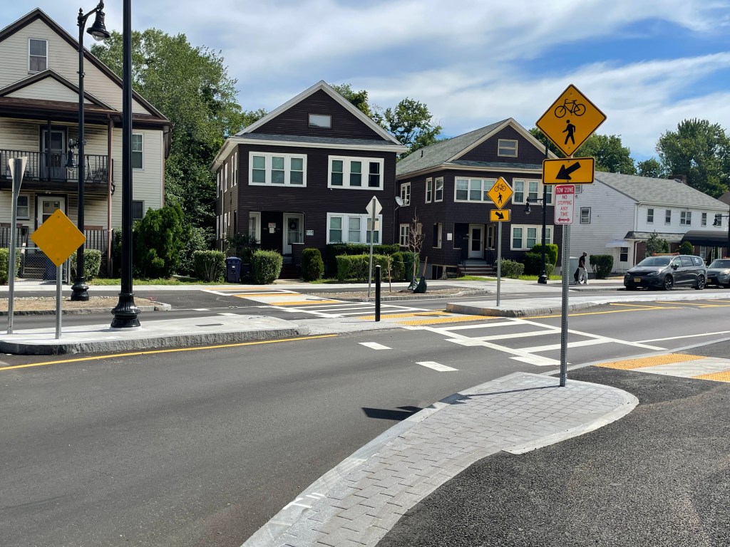 Crosswalks on the legs of a roundabout with a row of 2-3 story houses visible on the other side of the street.