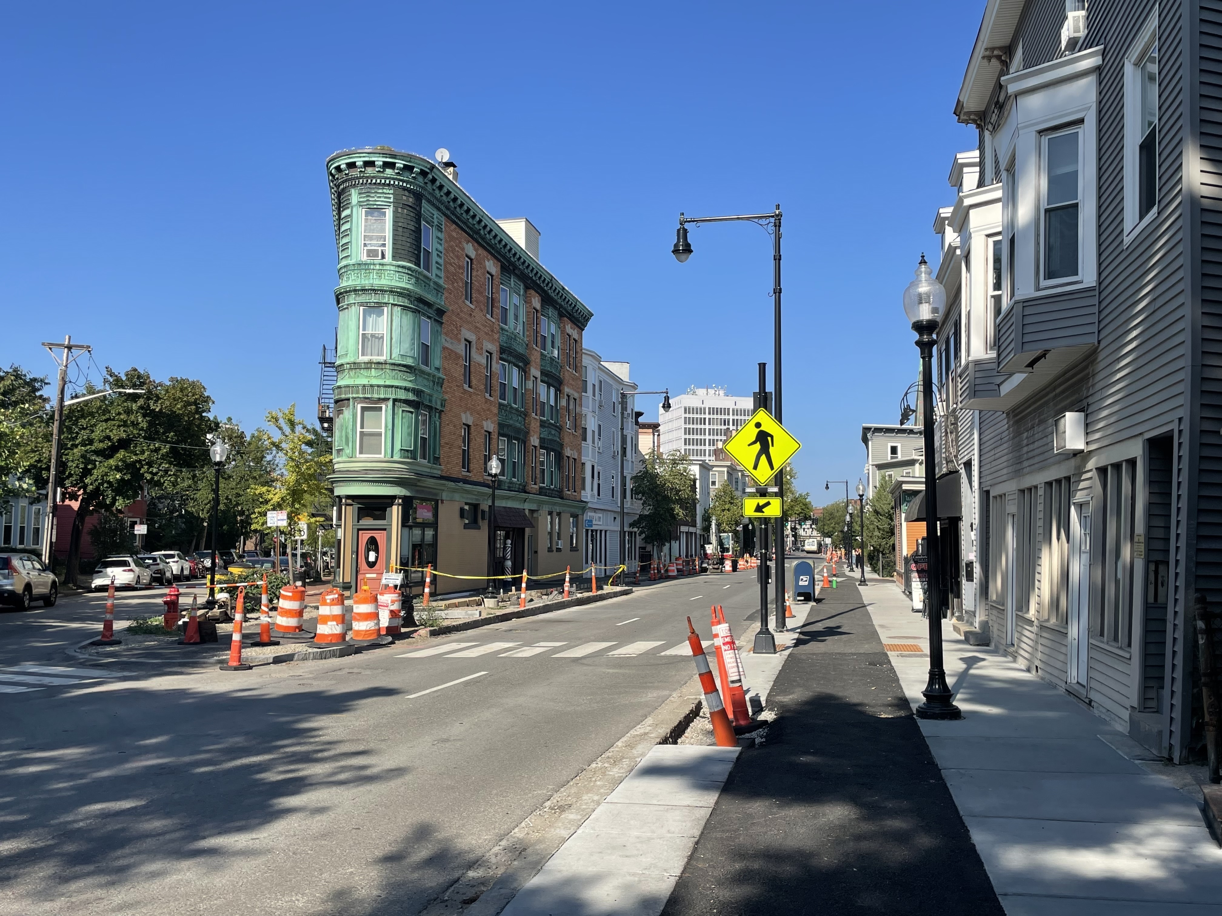 A street under construction with a sidewalk-level bike lane on the right side and a four-story flatiron building to the left.