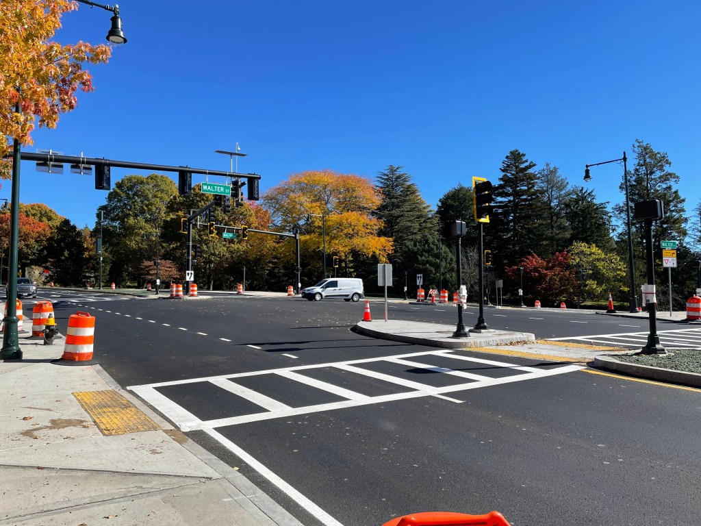 A crosswalk at the edge of a newly-paved intersection. A sign on the traffic light above the junction says "Walter St".