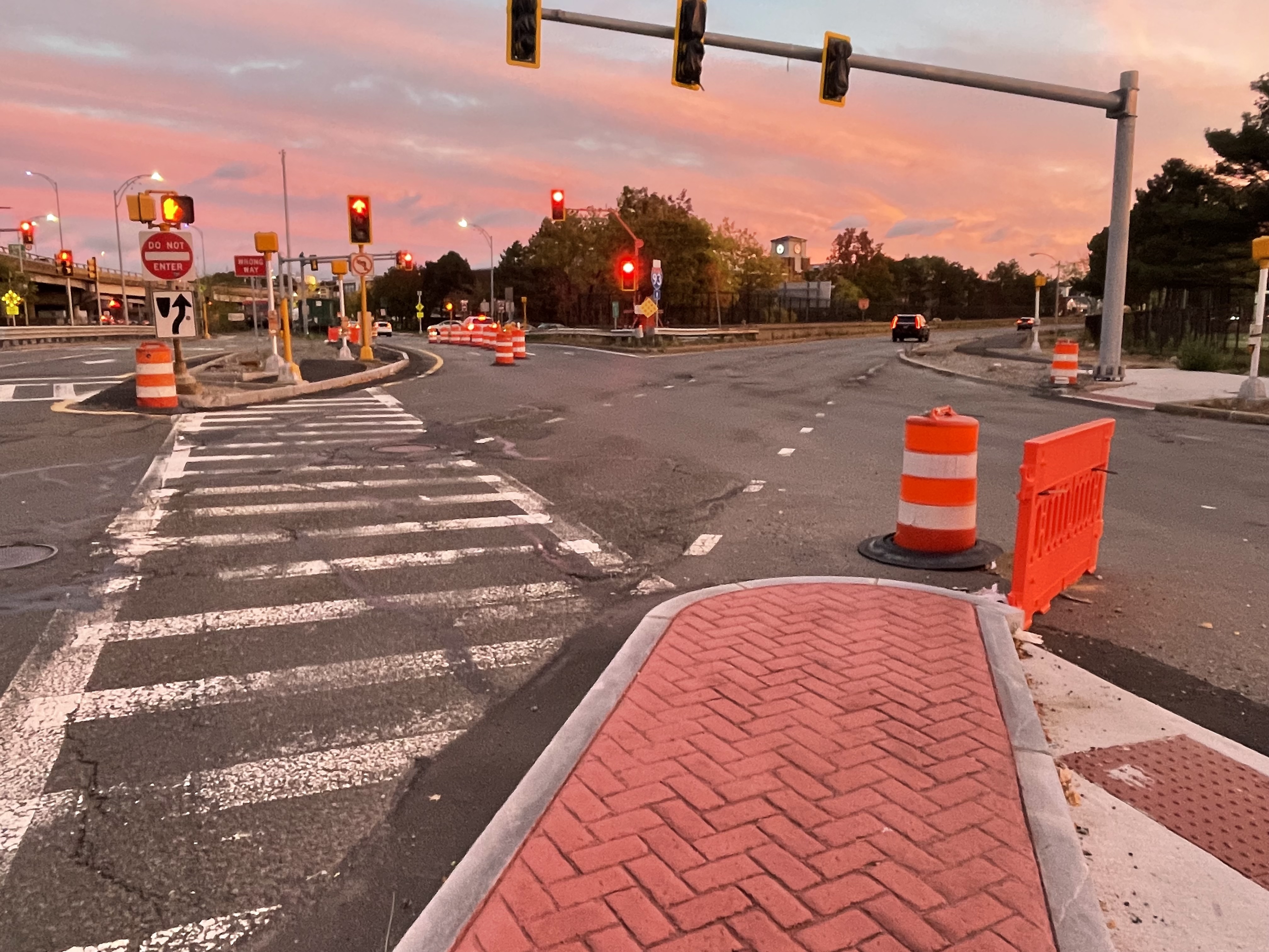 A photo of a complex intersection with numerous orange construction barrels and barriers at sunset. 